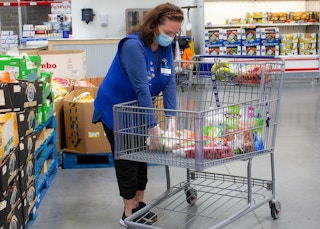 A Sam's Club employee wearing a face covering putting items inside a shopping cart for an order pick up
