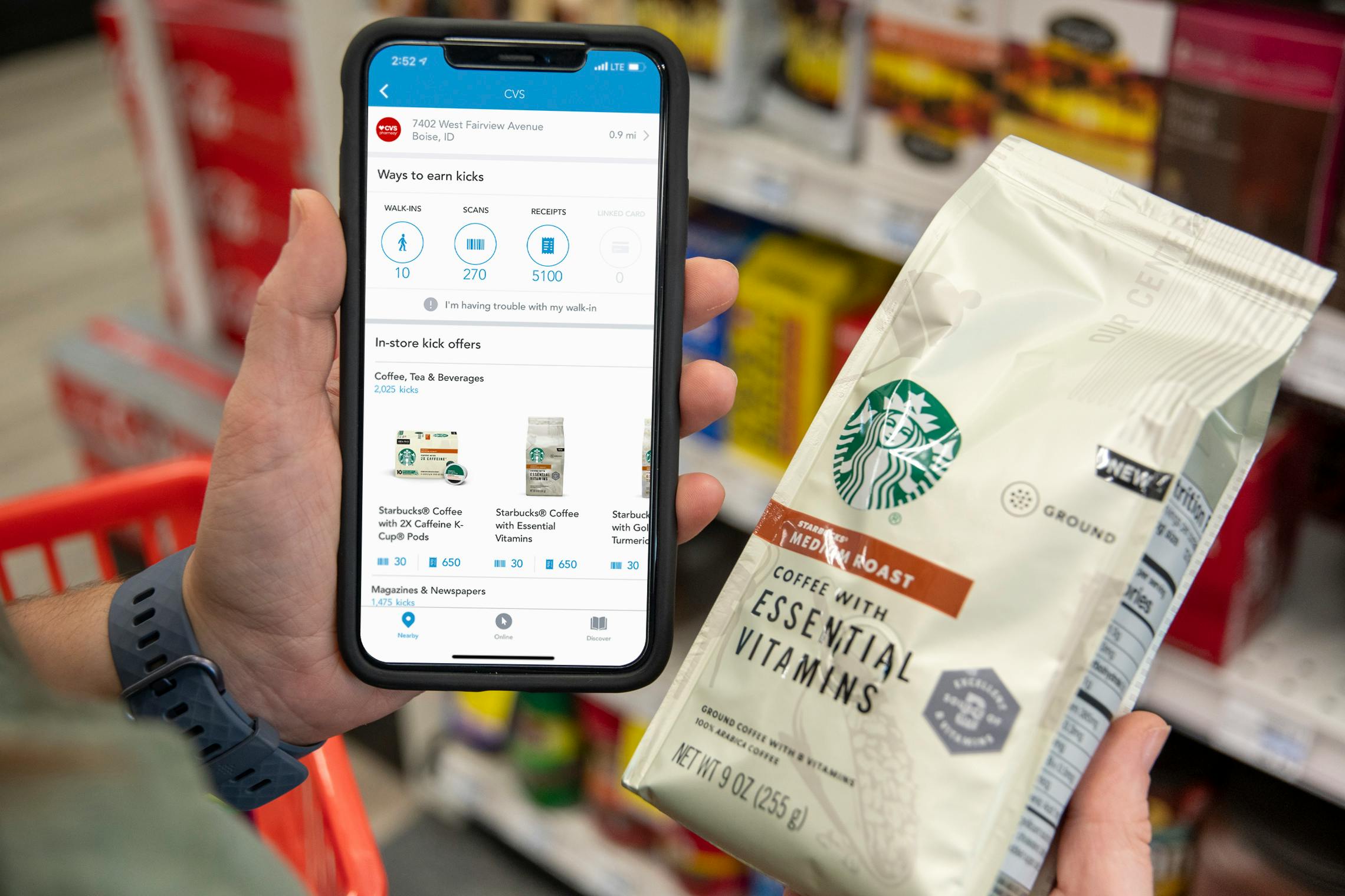 A person holding a bag of starbucks coffee next to a cell phone with the shopkick app on it.