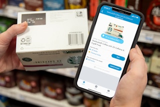 A person holding a box of starbucks coffee next to a cell phone with the shopkick app on it.