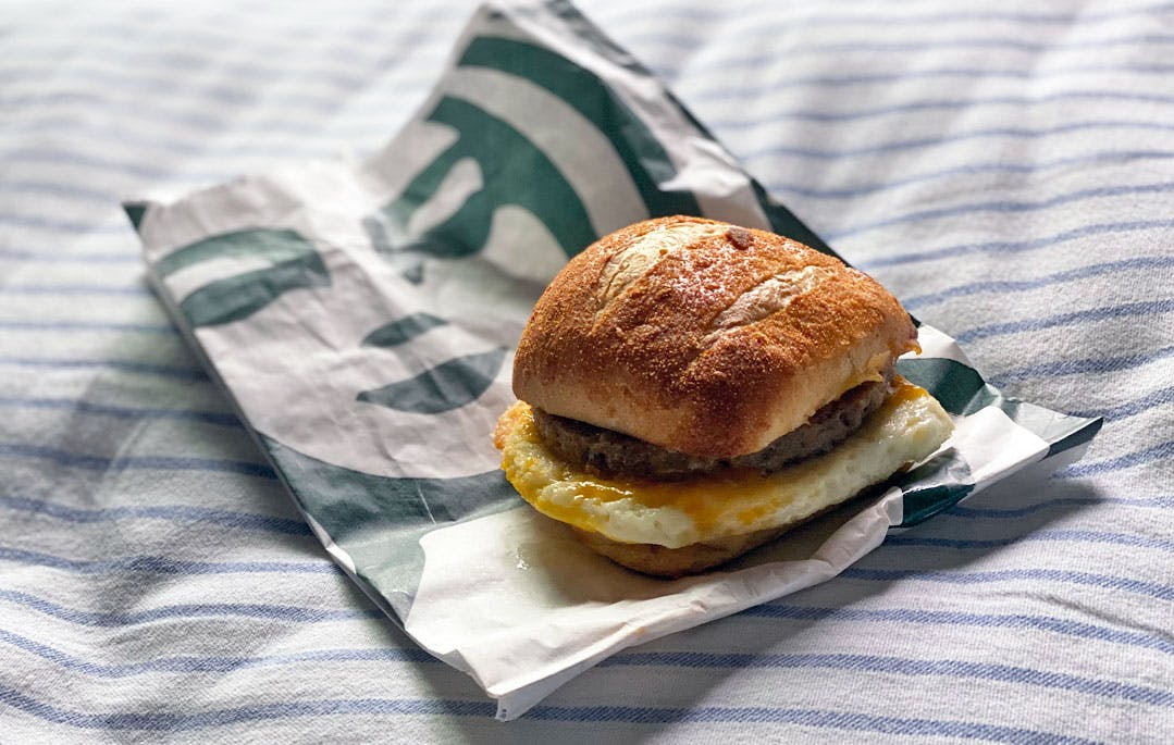A Starbucks Impossible breakfast sandwich sitting on its bag on a striped cushion.