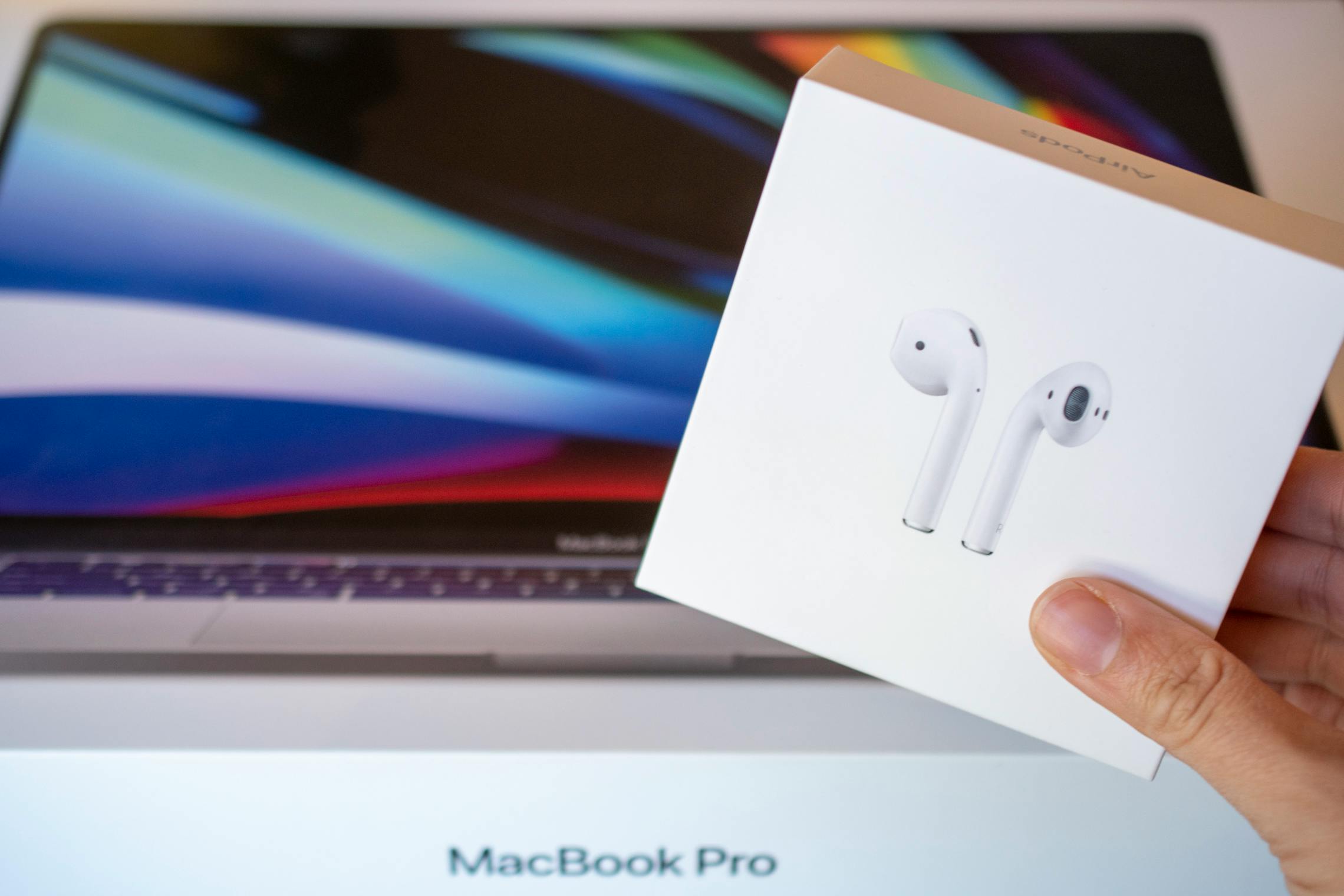 Apple airpods box held in front of a macbook pro laptop computer.