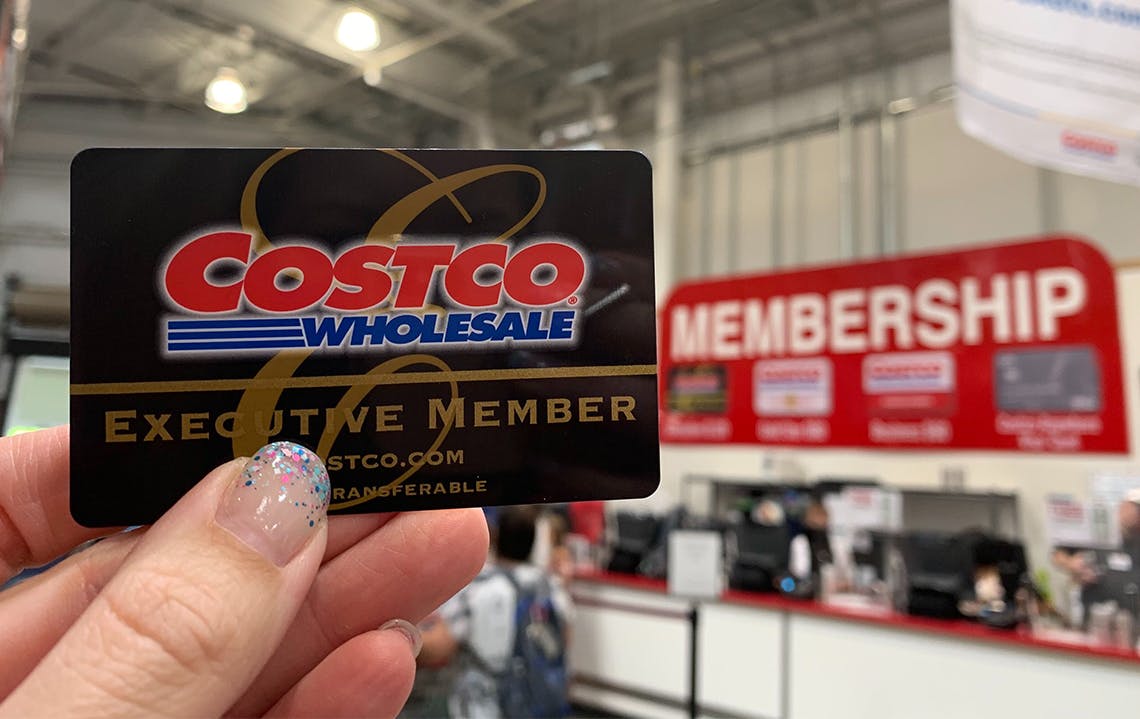 costco membership being held up to membership counter sign