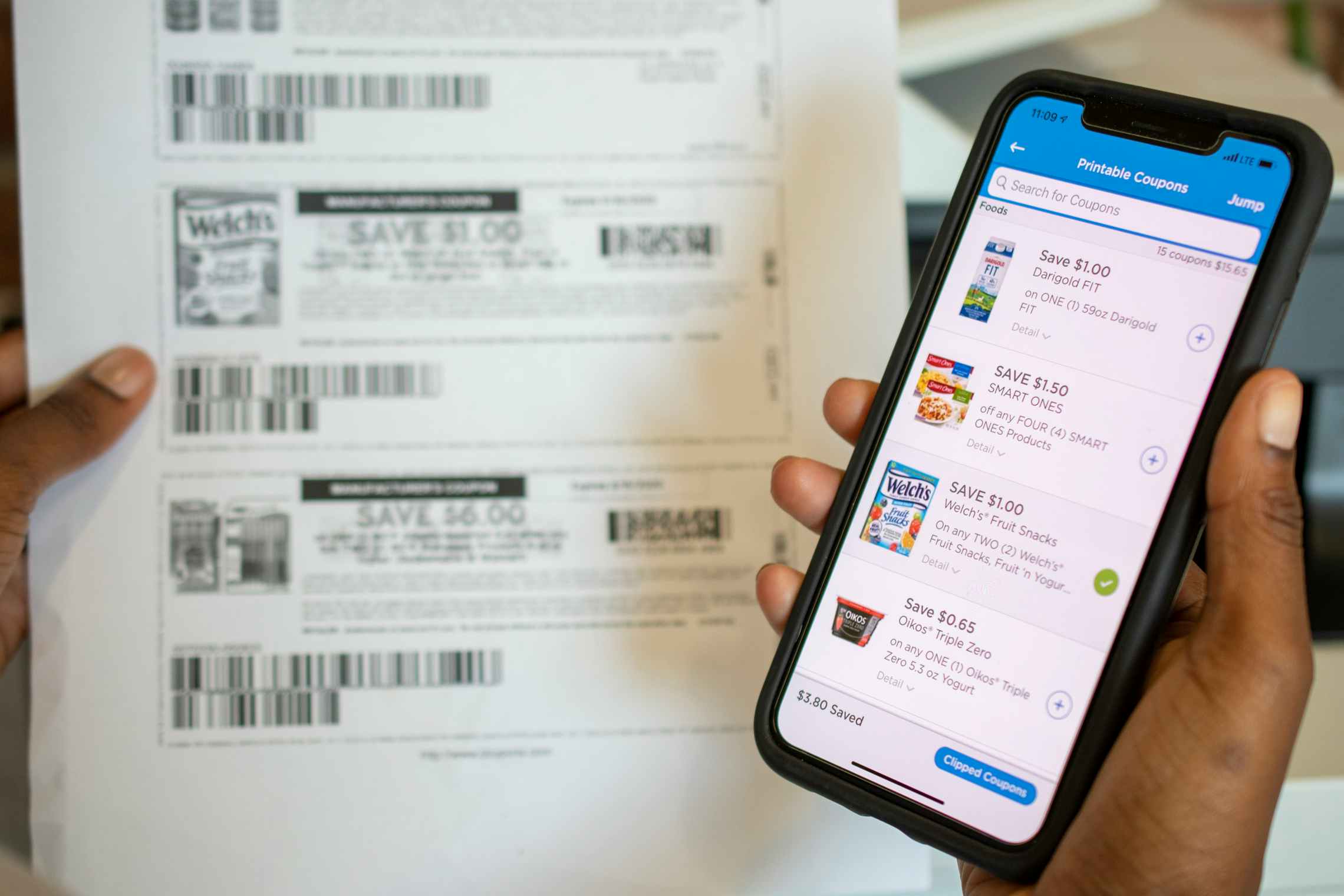 A person holding a smartphone in one hand while holding a sheet of printed coupons.