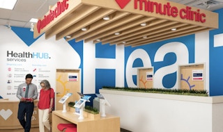 Two people walking past a desk at a CVS Minute Clinic health hub.
