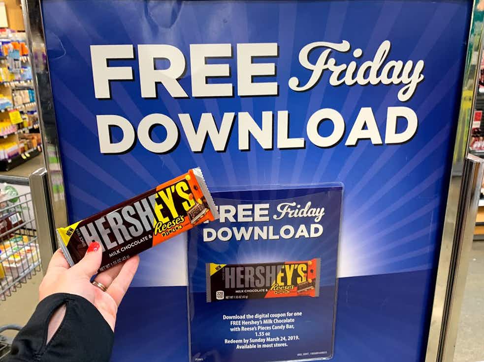A candy bar held in front of a Free Friday Download sign inside a Kroger store.