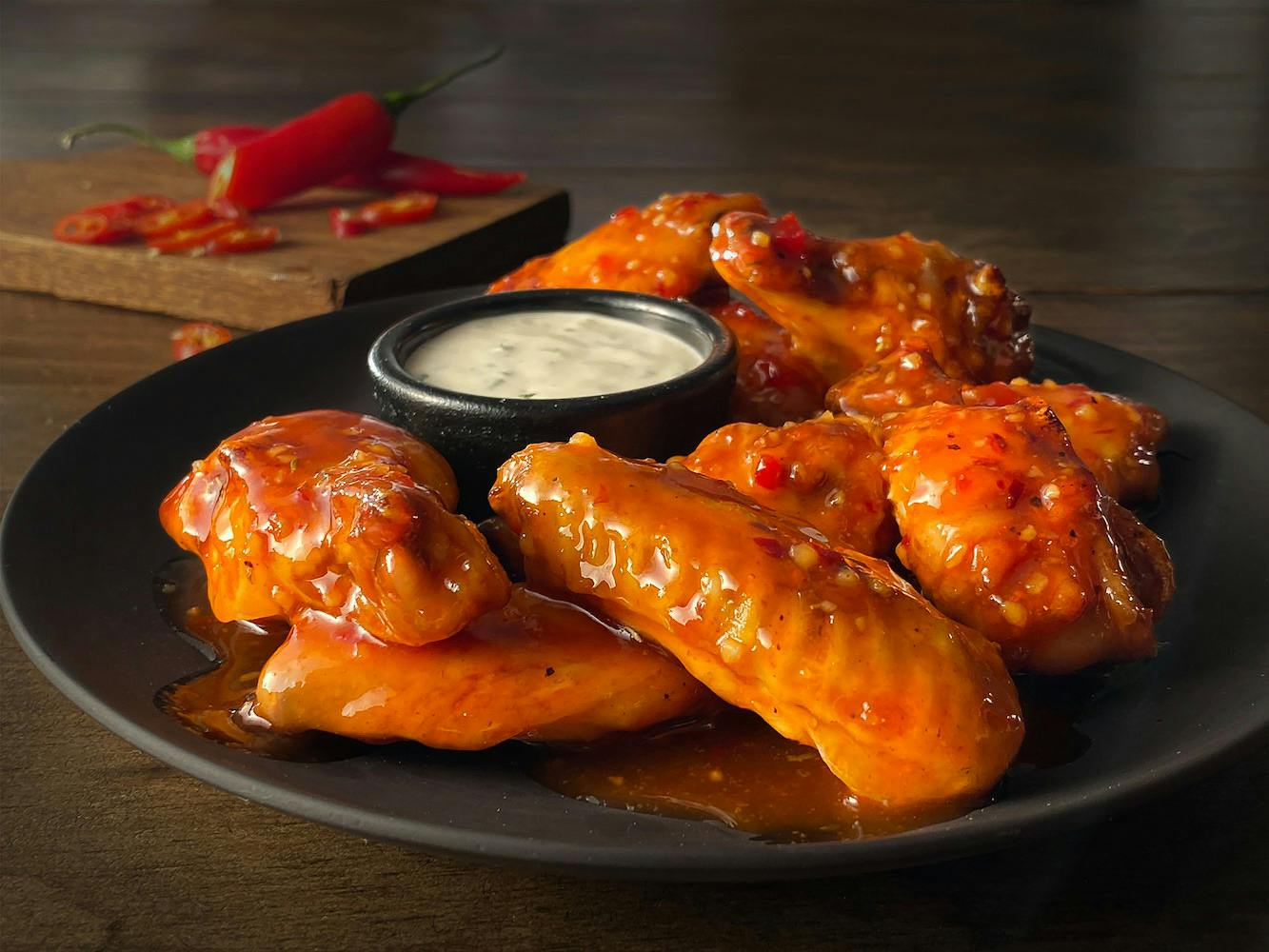 A plate of chicken wings from Hooters on a table with a ranch dipping cup and a pepper cut on a cutting board in the background.