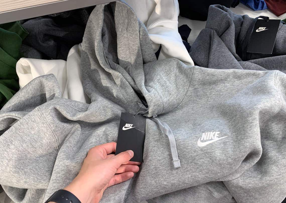 A person's hand holding the tag of a Nike sweatshirt laying on a shelf.