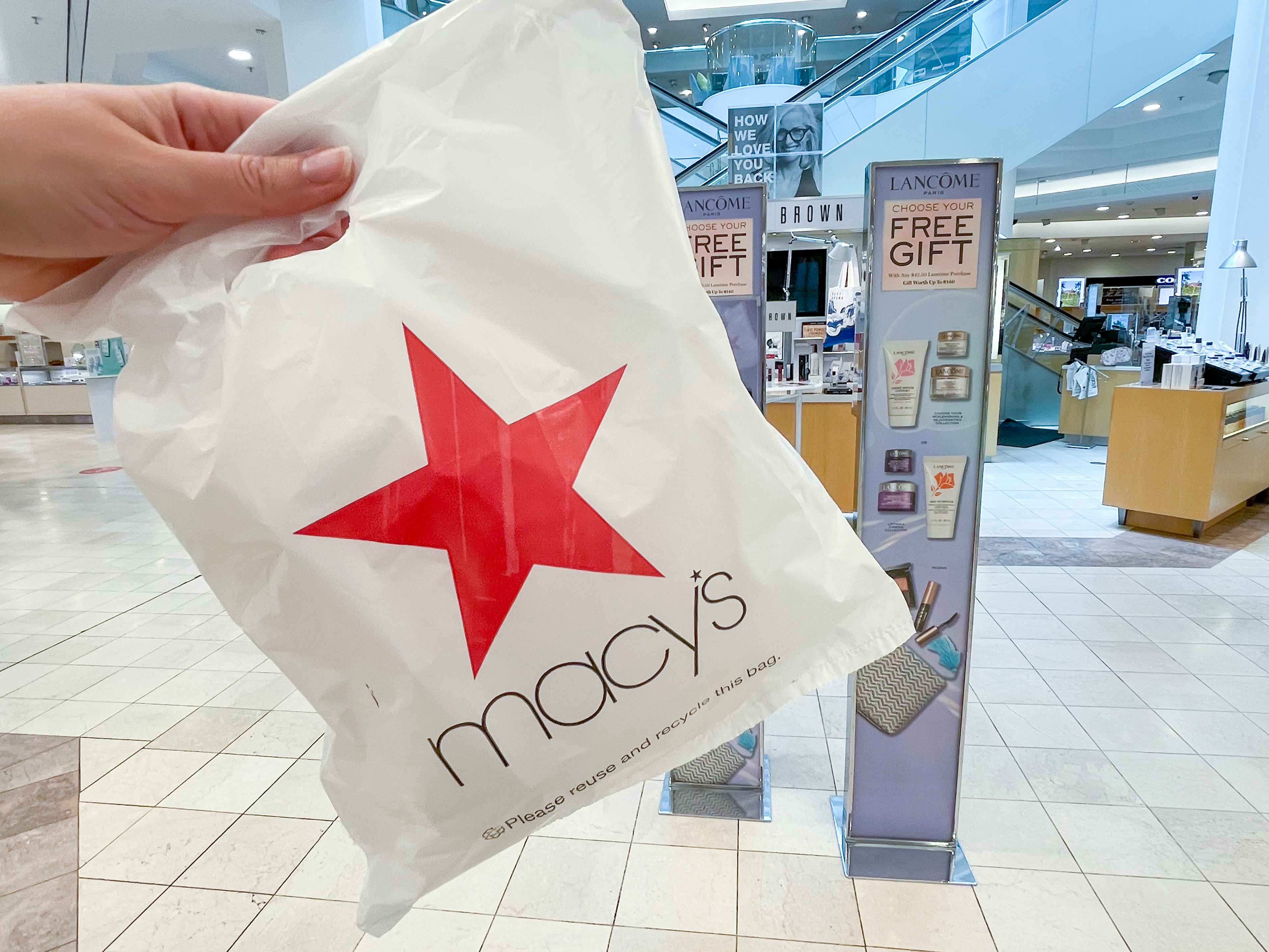 Macy's shopping bag held in front of the cosmetic section.