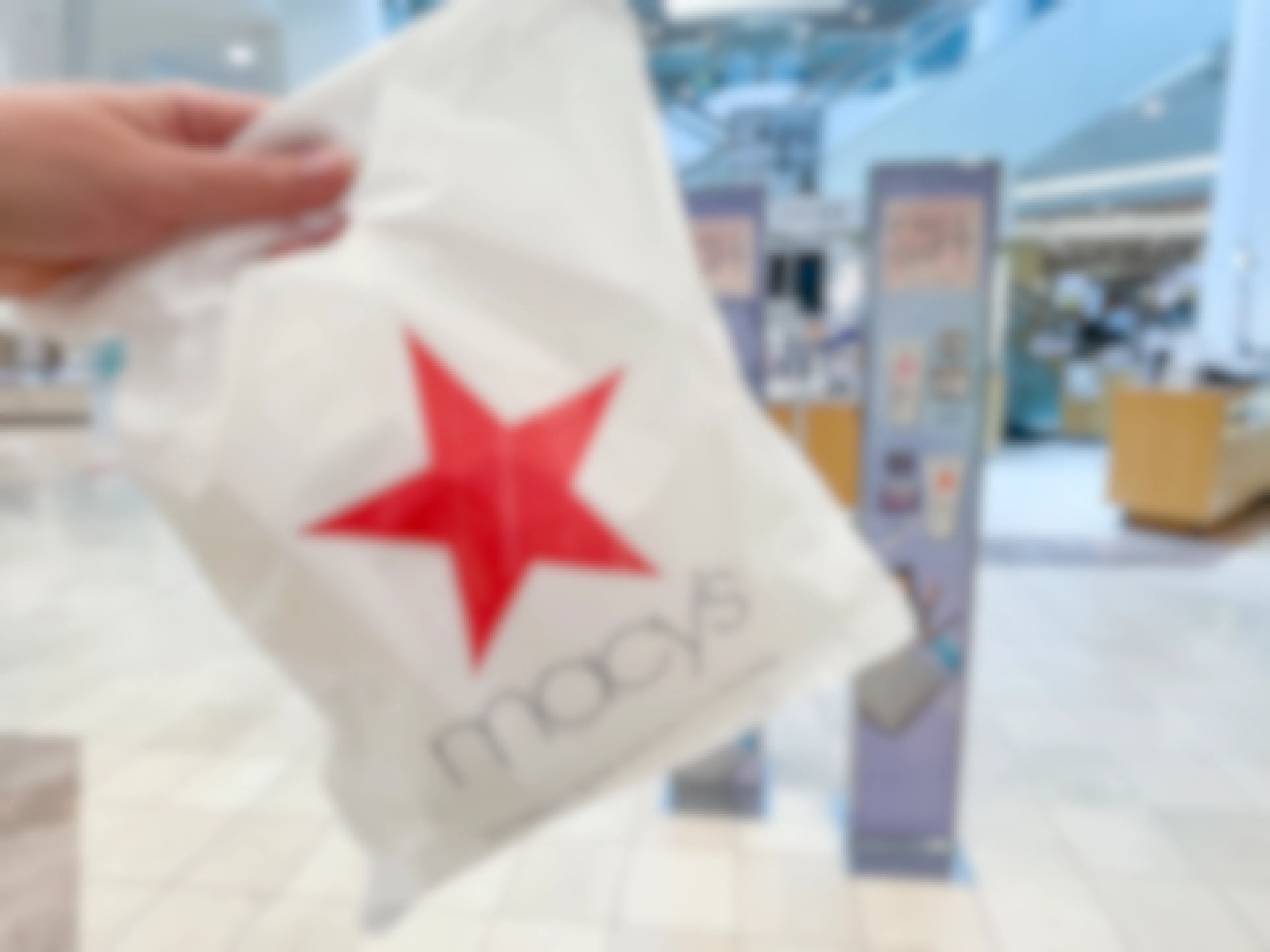 Macy's shopping bag held in front of the cosmetic section.