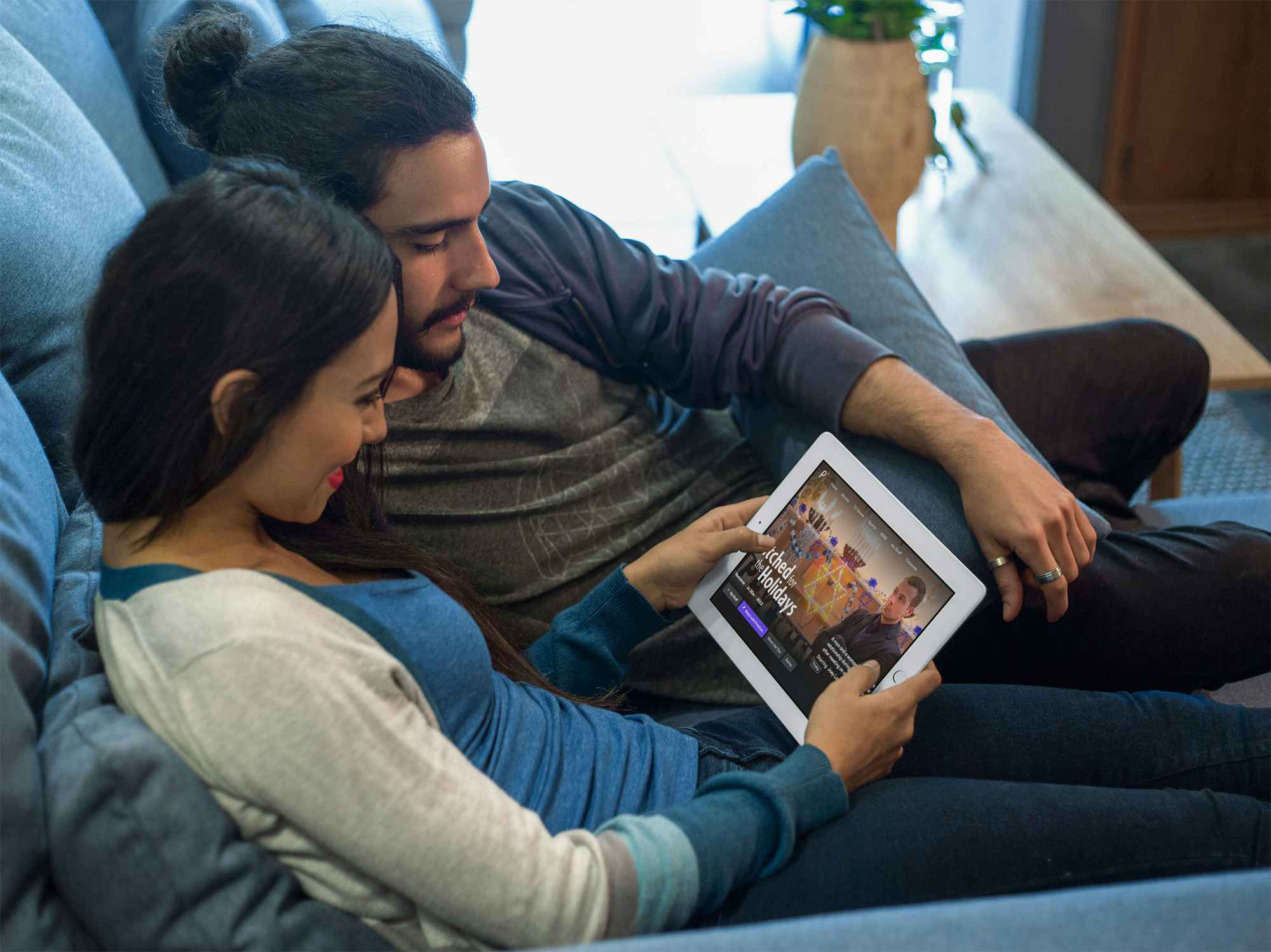 A couple sitting together on a couch, picking a Hallmark movie to watch on the Peacock app