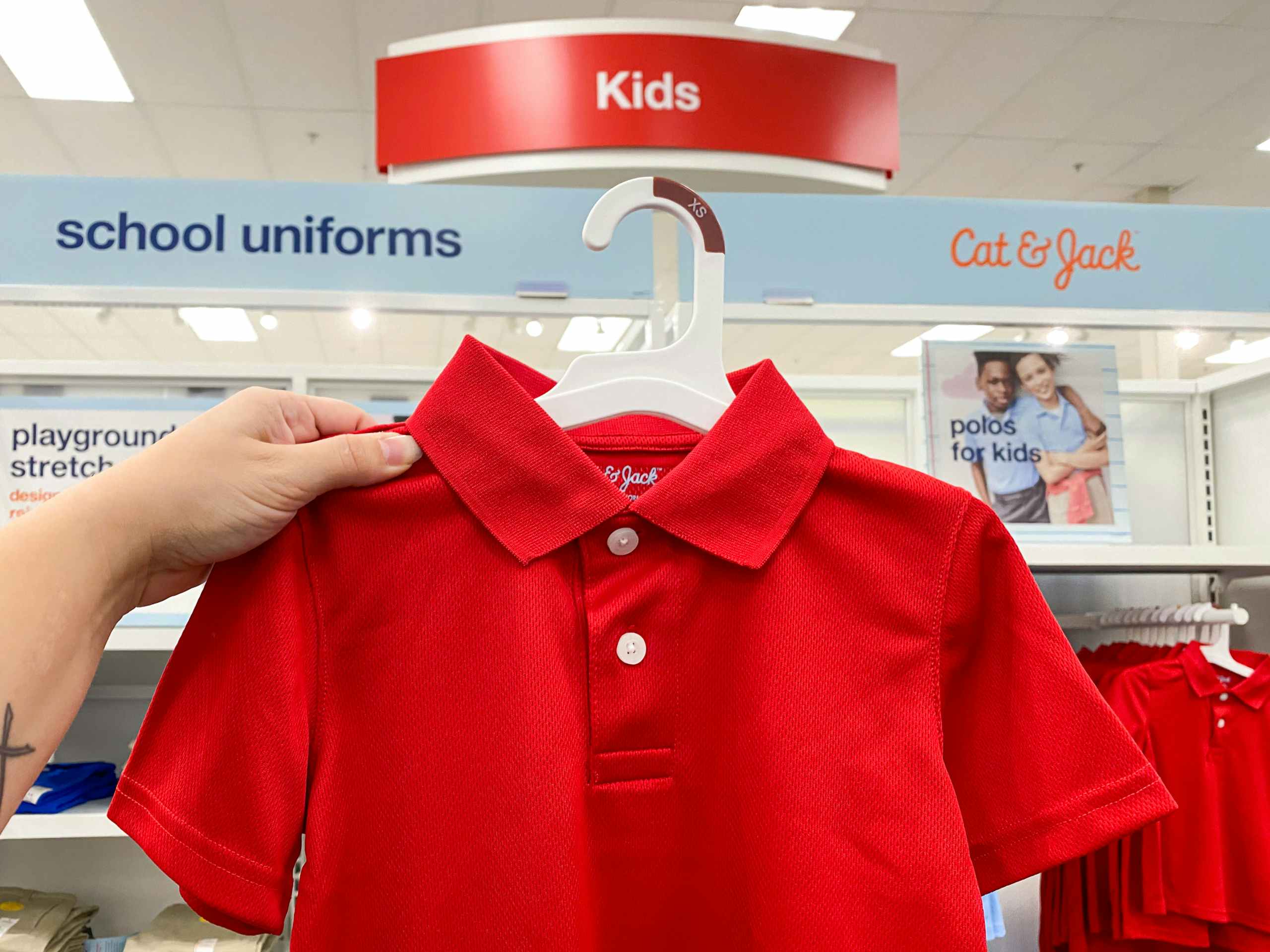 A person's hand holding up a Cat & Jack kids school uniform polo in front of the school uniform section signage at Target.