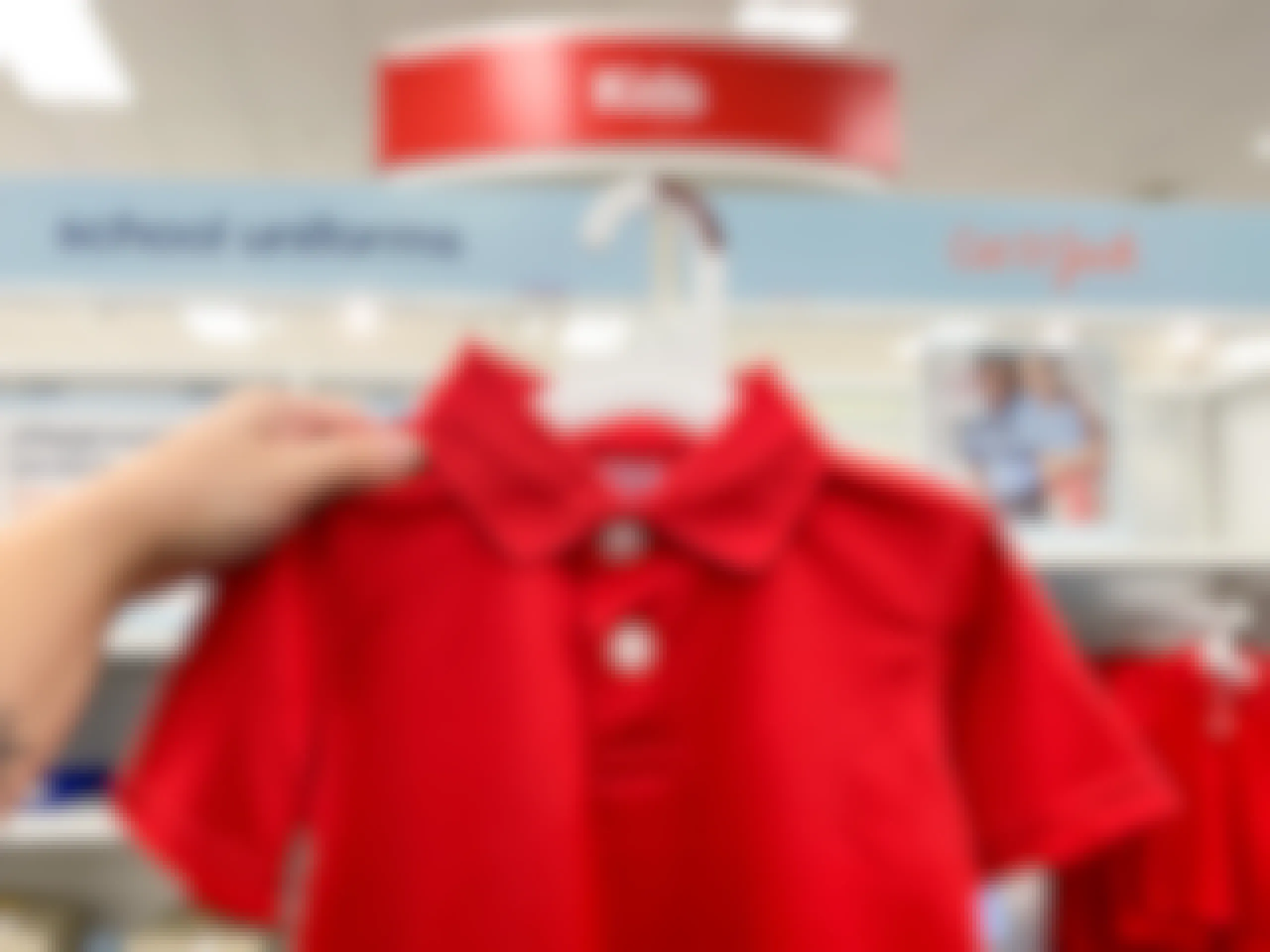 A person's hand holding up a Cat & Jack kids school uniform polo in front of the school uniform section signage at Target.