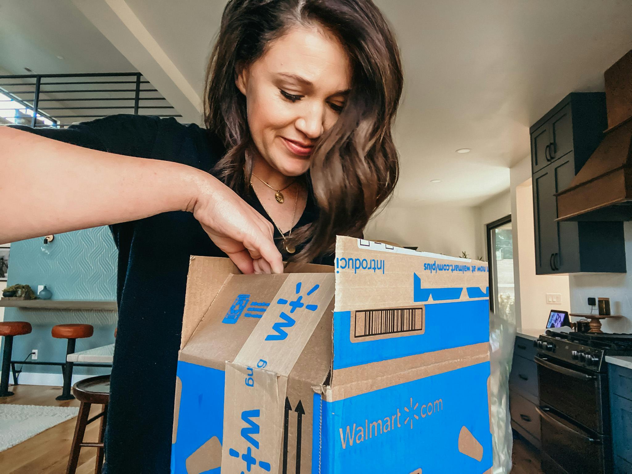 A woman opening a Walmart+ box in her kitchen.