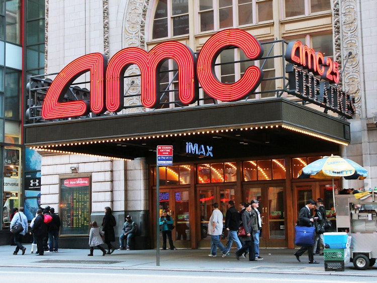 An AMC movie theater entrance with people walking by on the sidewalk.