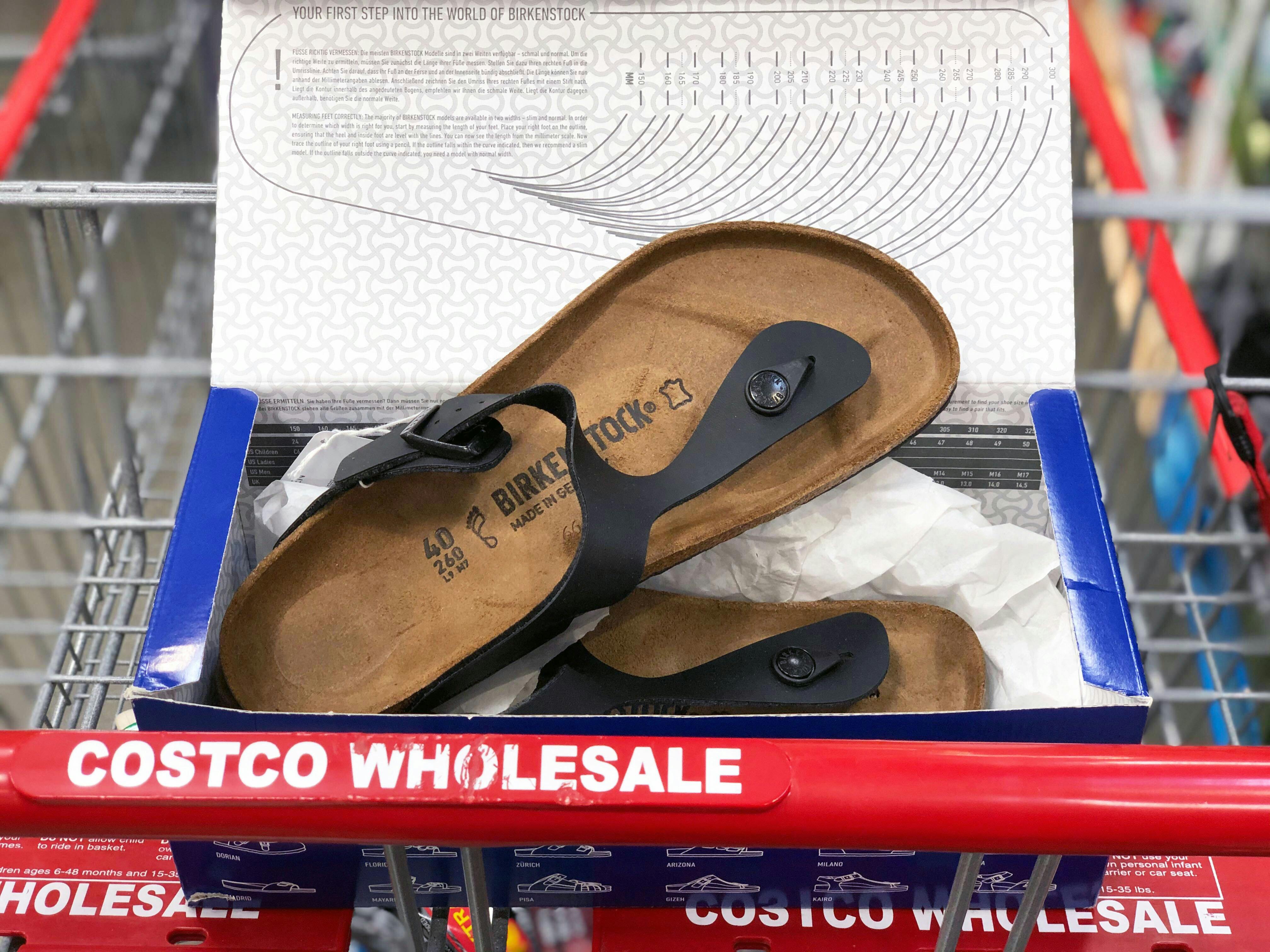 A pair of Birkenstock sandals in a shoebox sitting in the basket of a Costco shopping cart.