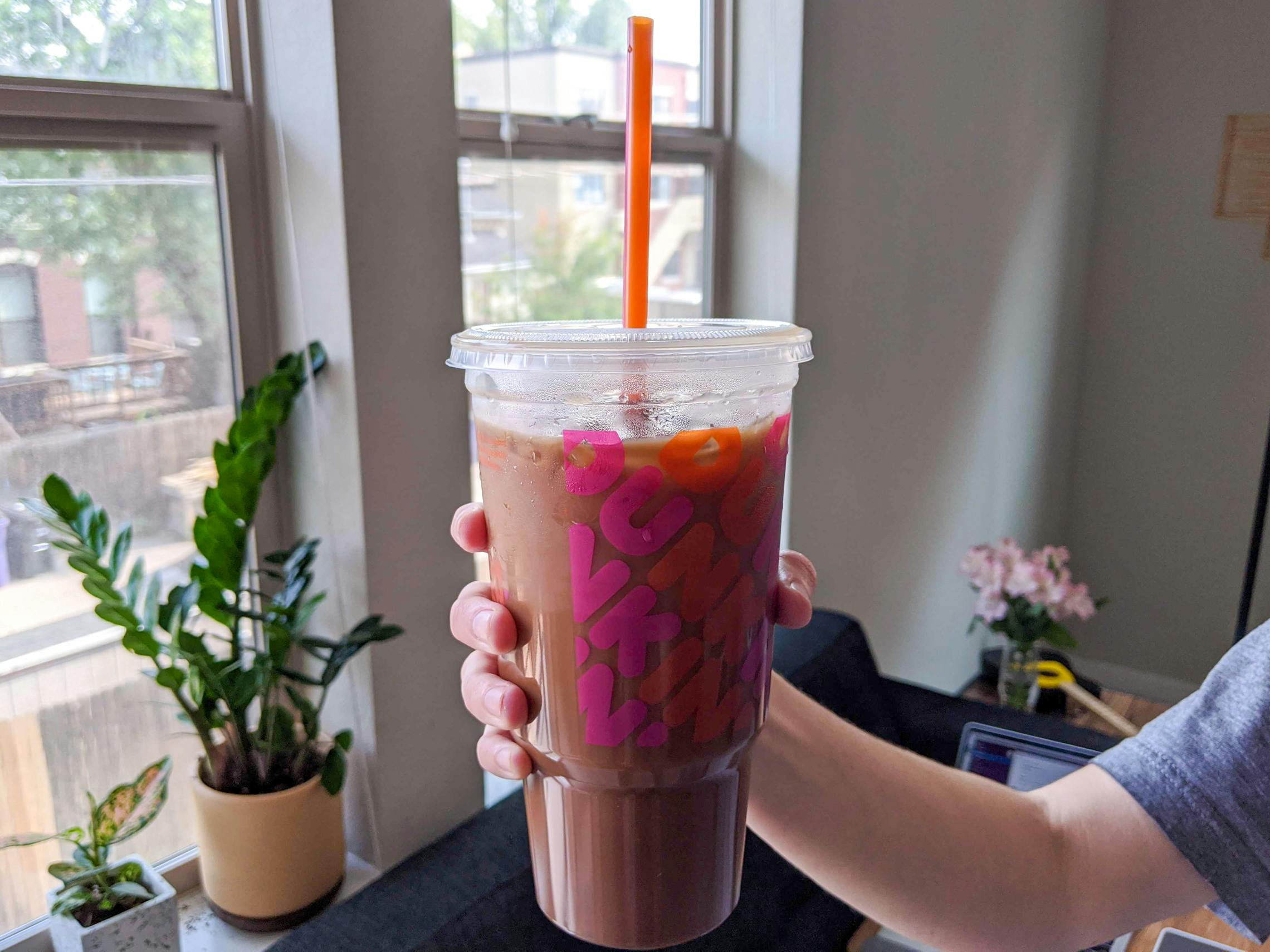 A person holding a large iced coffee from Dunkin' Donuts.