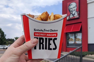 KCF secret menu fries, cheese curds, and brown gravy poutine, held in front of a KFC restaurant.