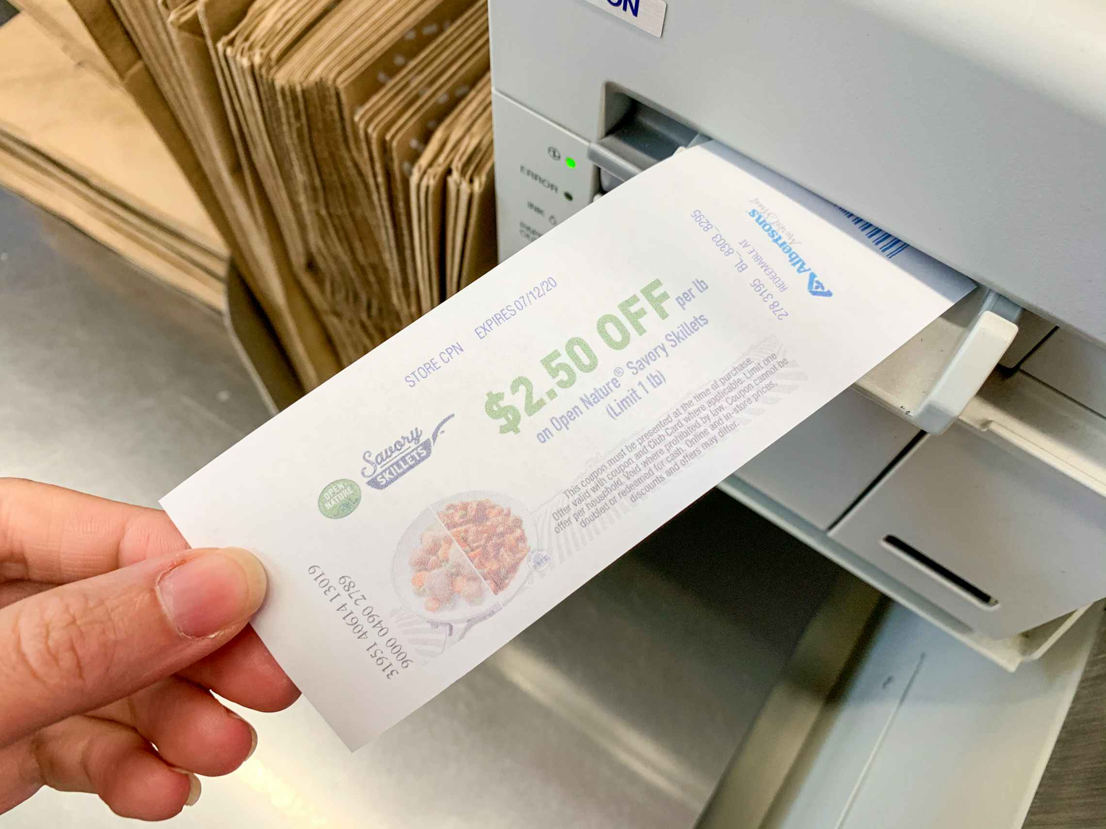 A person's hand pulling a printed Catalina coupon from the machine at a checkout register.
