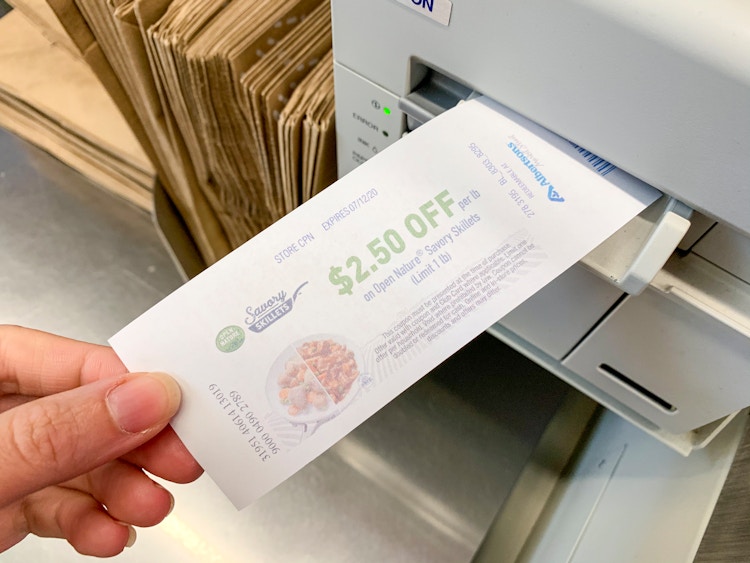 A person's hand pulling a printed Catalina coupon from the machine at a checkout register.