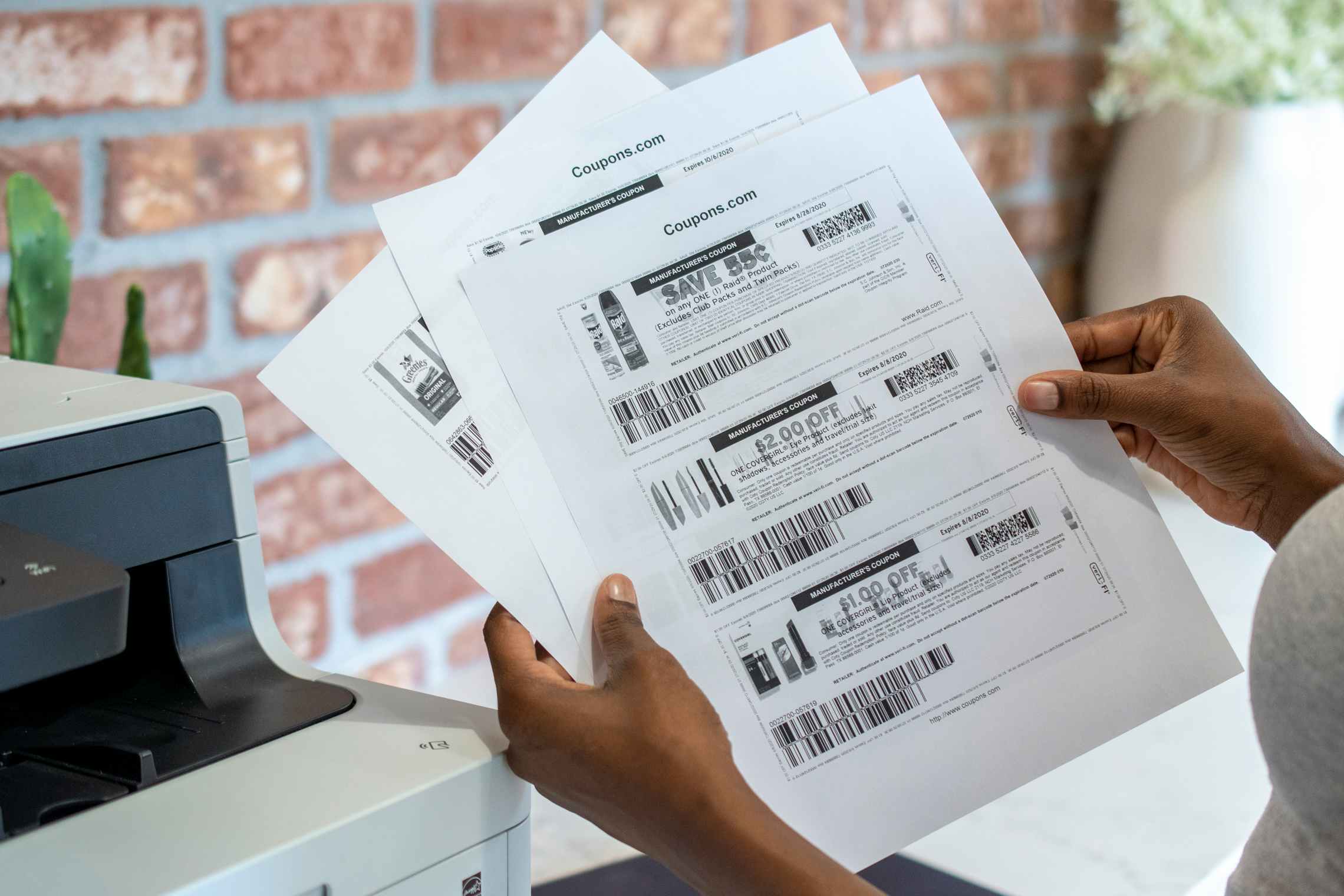A person holding black and white printed coupons next to a printer.