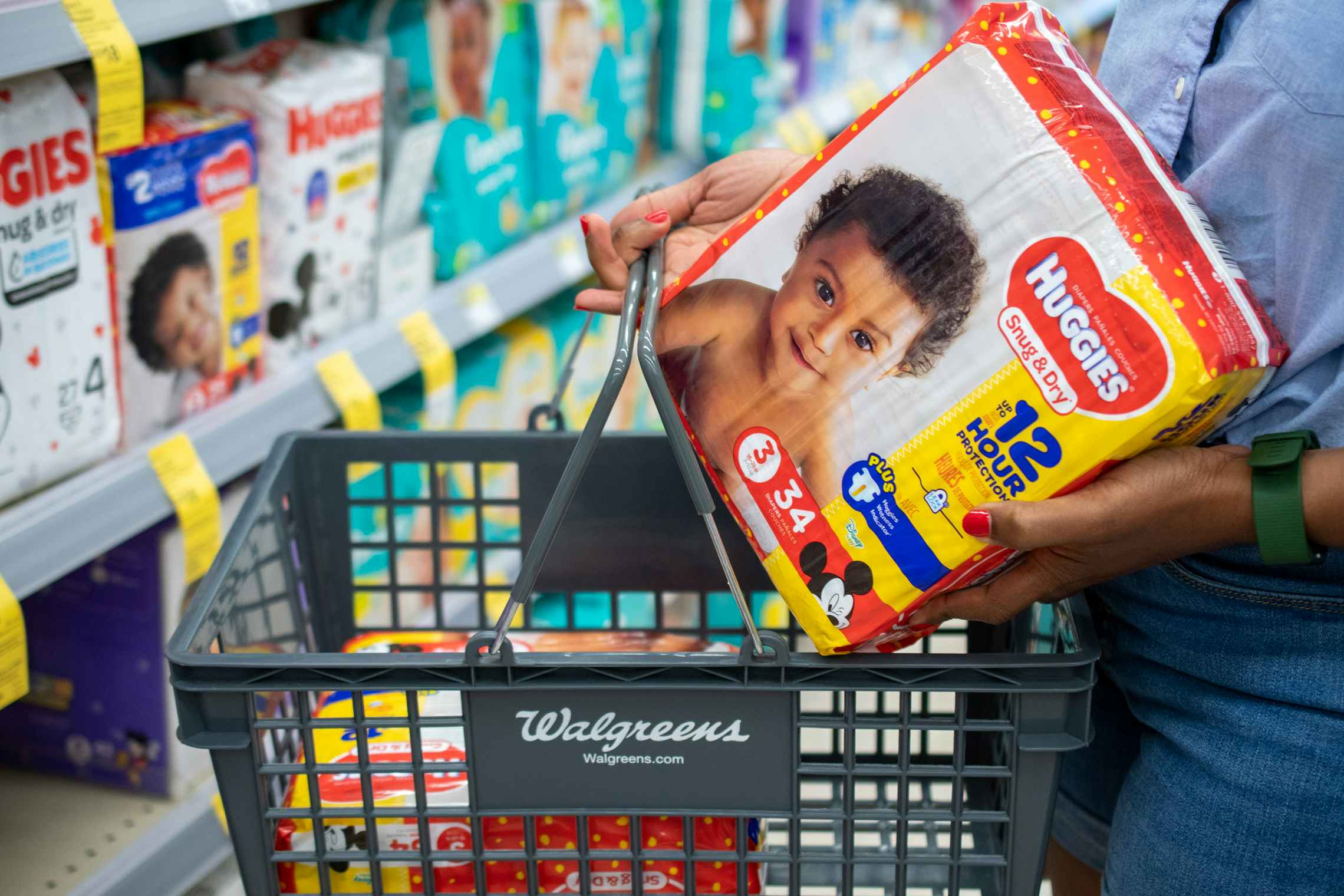 A woman putting a pack of Huggies Daipers into a hand basket inside Walgreens