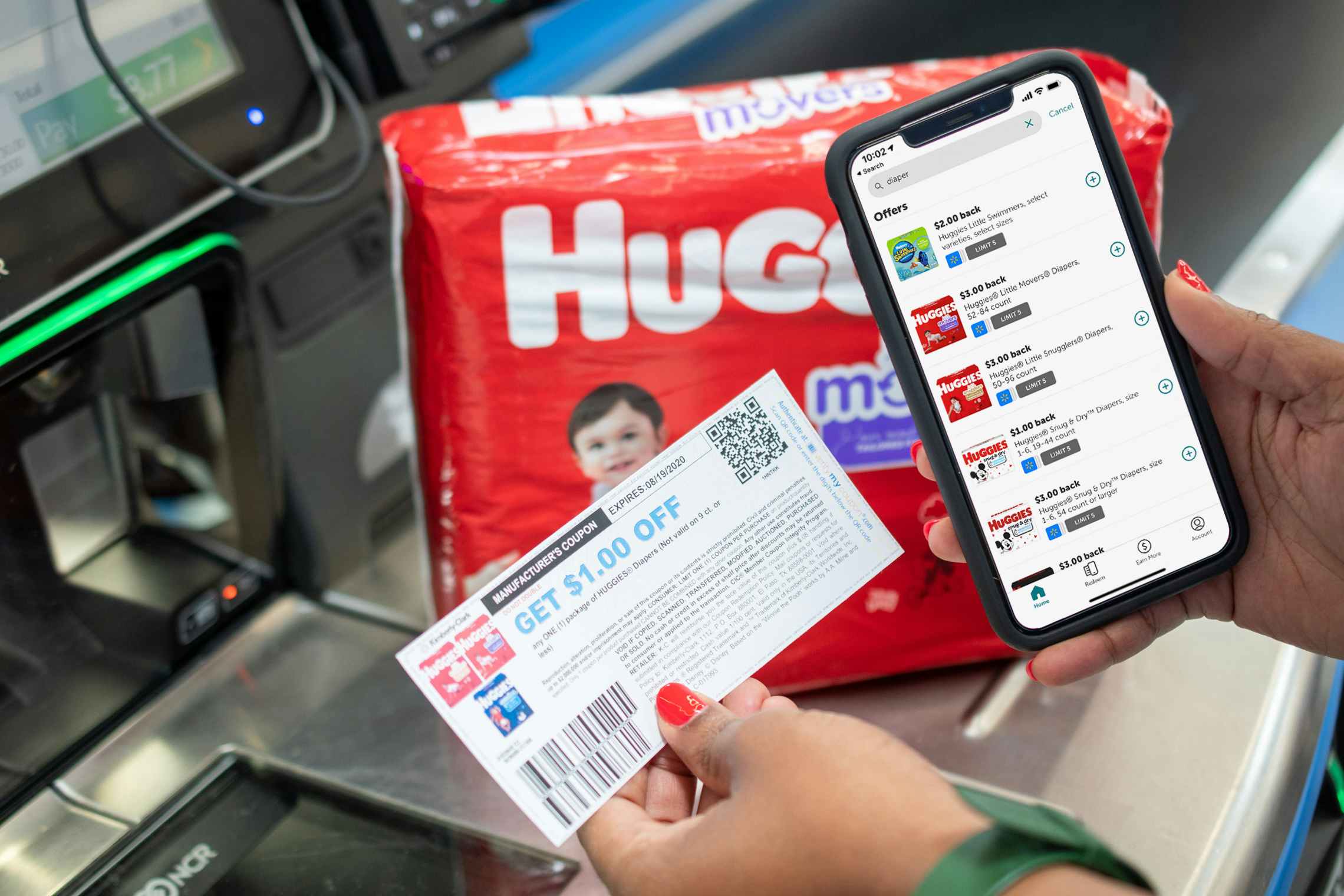 Ibotta app on a cell phone next to coupons and Huggies diapers at a Walmart checkout stand.