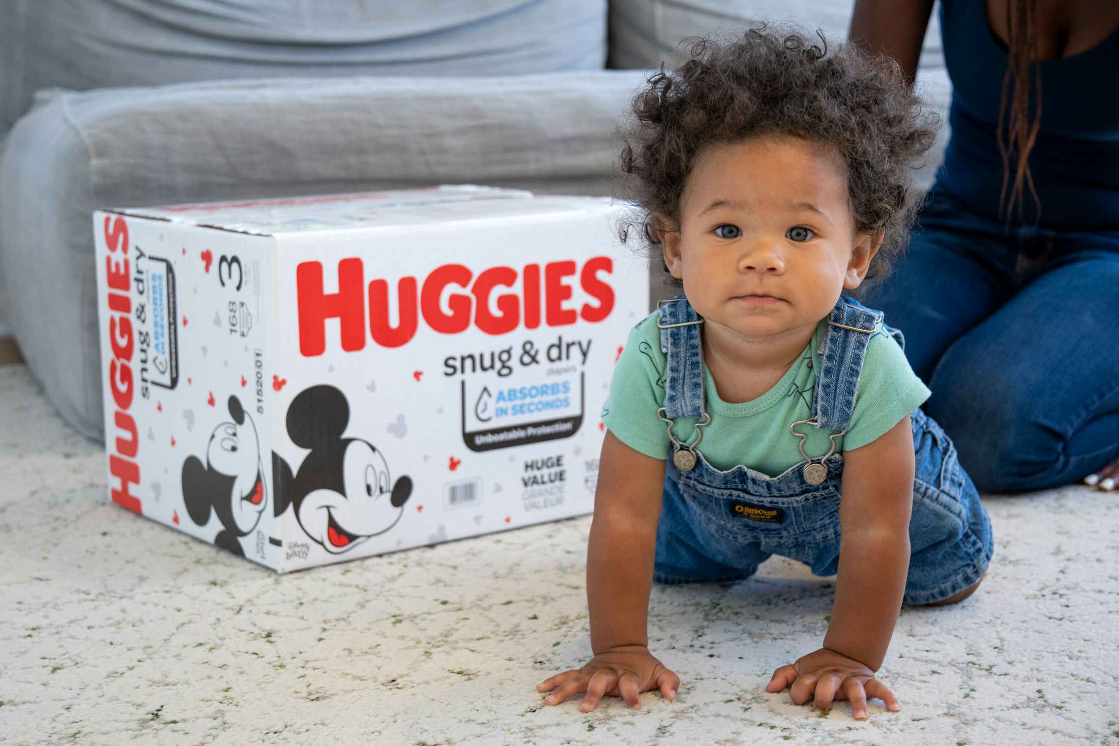 A little boy crawling next to a huggies diaper box.