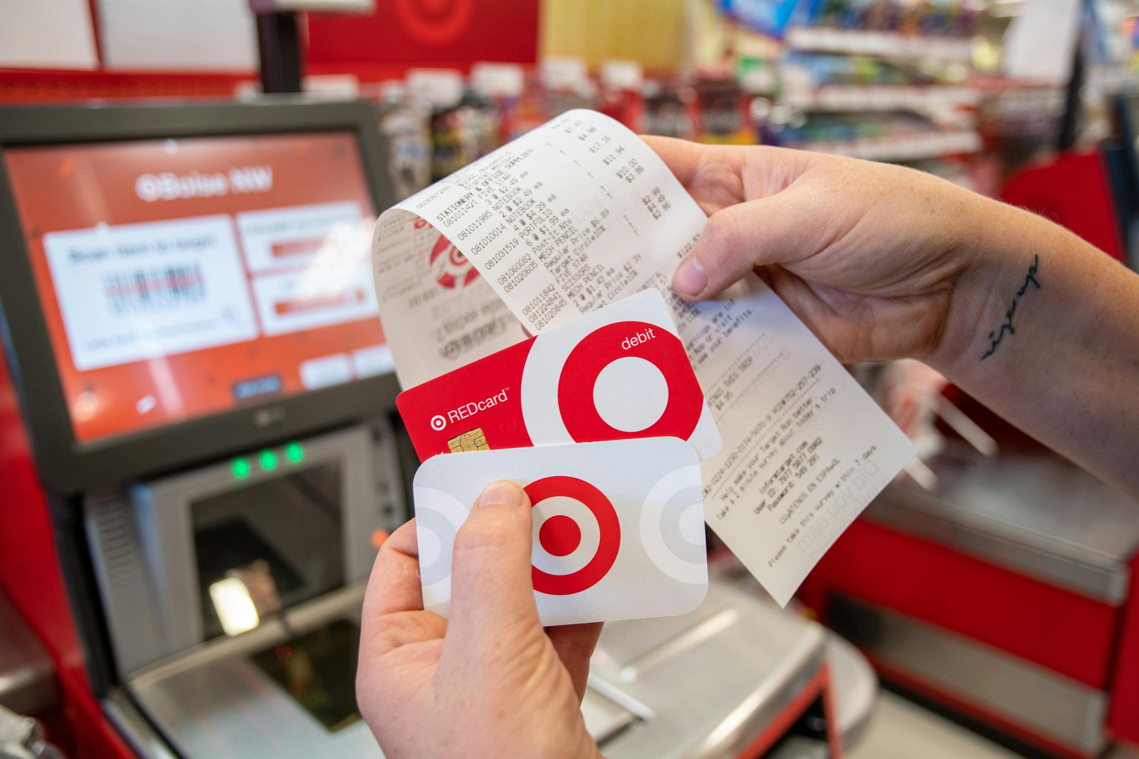 A person's hands holding up a Target gift card, a Target Red Card, and a receipt in front of the self-checkout scanner at Target.