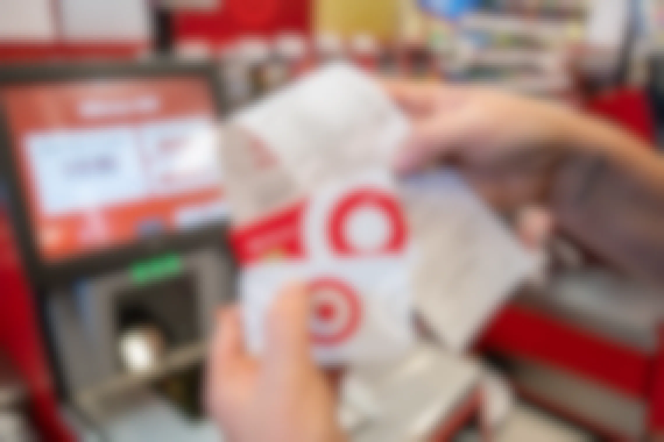 A person's hands holding up a Target gift card, a Target Red Card, and a receipt in front of the self-checkout scanner at Target.