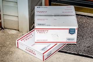 Two USPS Priority Mail boxes sitting on door mat at a front door.