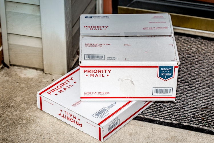 Two USPS Priority Mail boxes sitting on door mat at a front door.