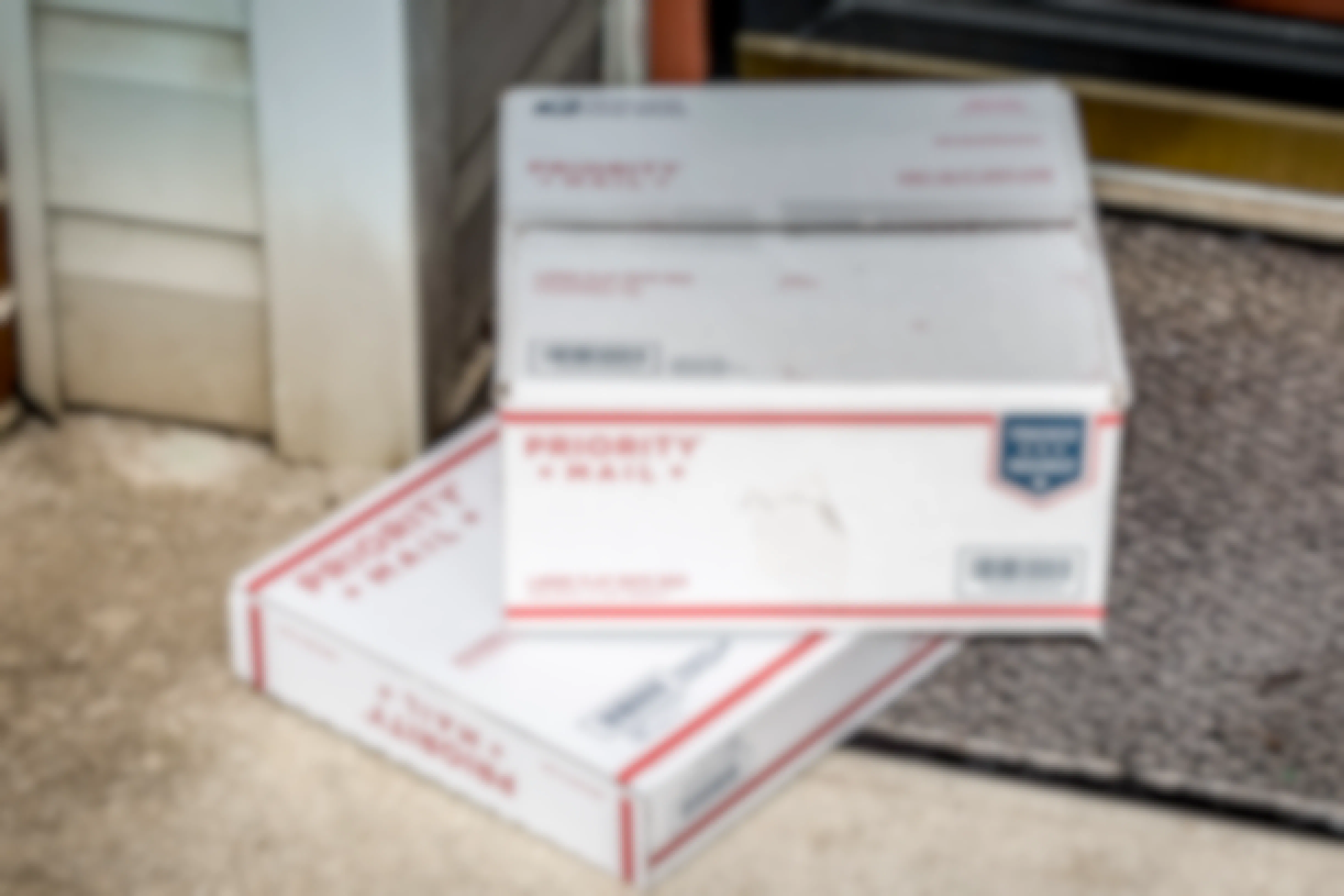 Two USPS Priority Mail boxes sitting on door mat at a front door.