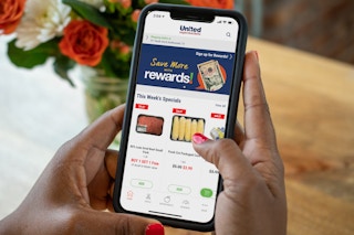 A person holding an iphone with the United Supermarkets app on the screen.