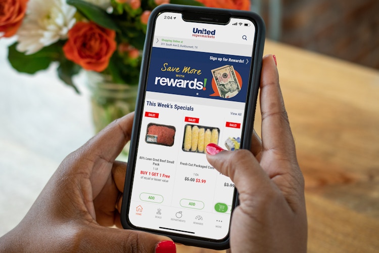 A person holding an iphone with the United Supermarkets app on the screen.