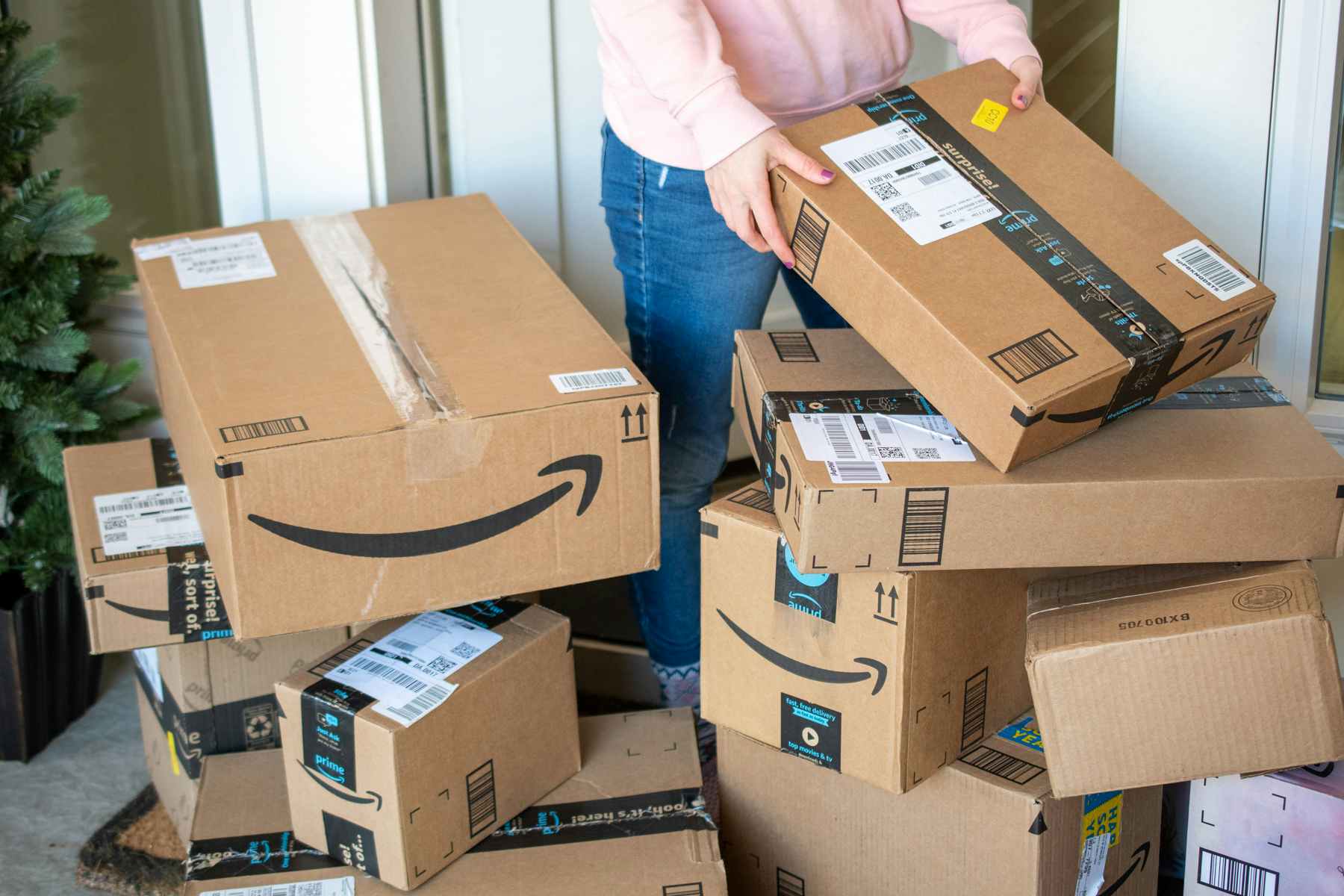 A woman collecting a pile of delivery boxes from a doorstep.