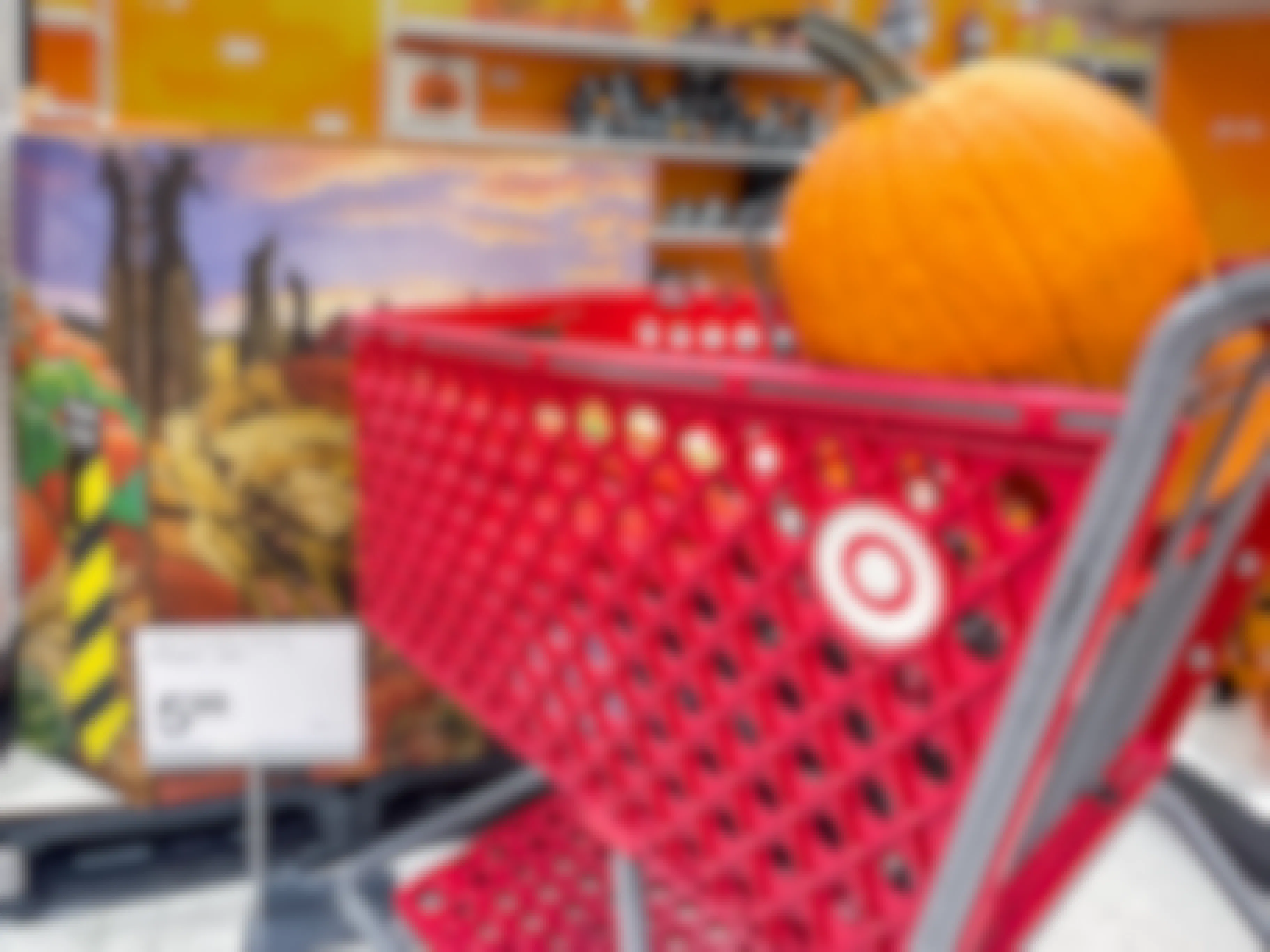 A pumpkin in a Target shopping cart parked next to a large box of more pumpkins and a sign that shows the price to be $5.99