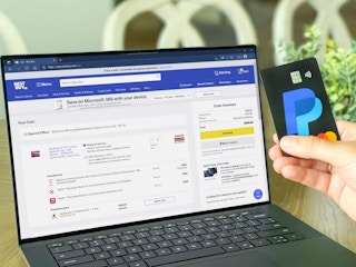 laptop with best buy shopping cart with a paypal card being held next to it