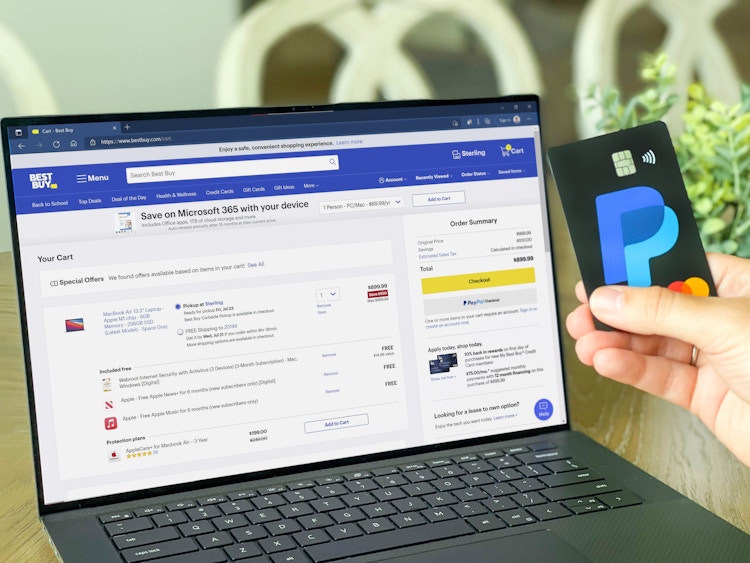 laptop with best buy shopping cart with a paypal card being held next to it