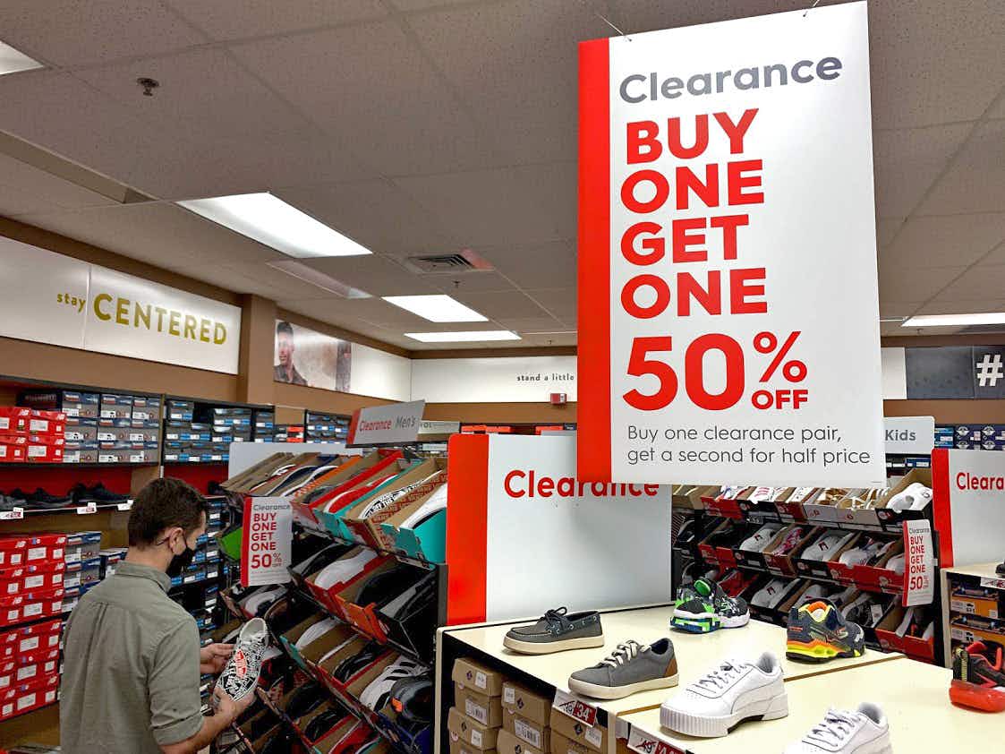 Man shopping in the clearance aisle in famous footwear with a sign above that reads "clearance buy one get one 50%off