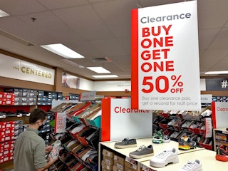Man shopping in the clearance aisle in famous footwear with a sign above that reads "clearance buy one get one 50%off