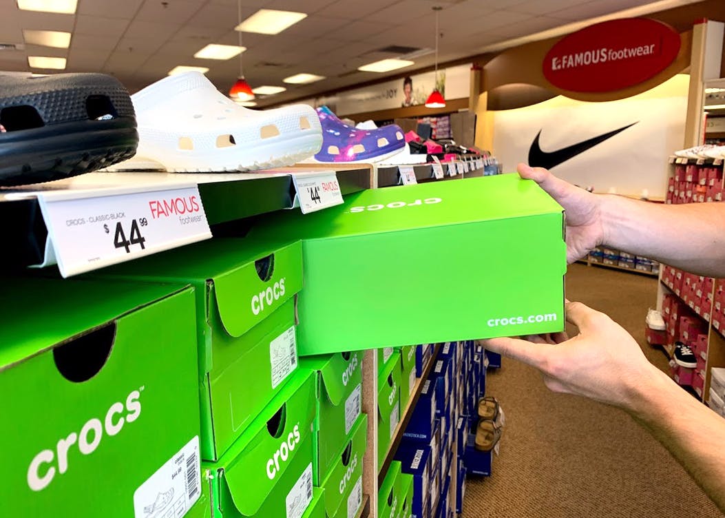 A person's hands taking a Crocs shoe box off of a shelf at Famous Footwear.