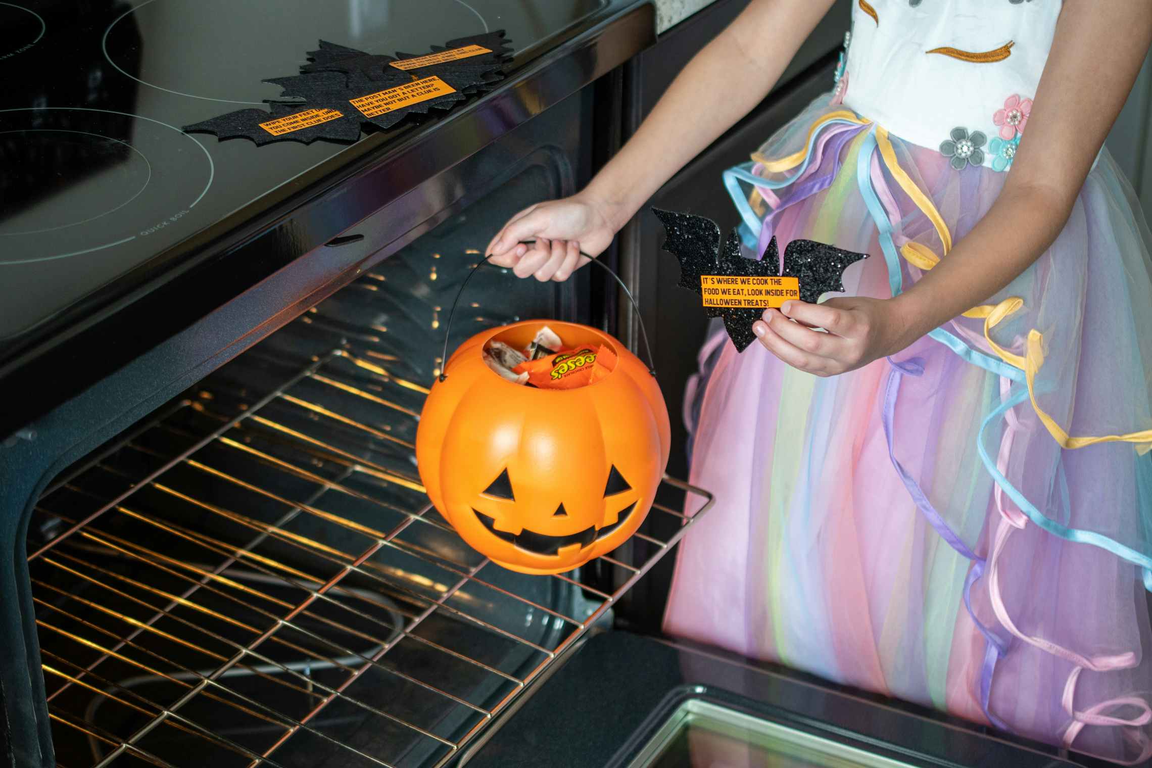 A little girl holding a scavenger hunt clue and pulling a pumpkin pail filled with candy from an oven