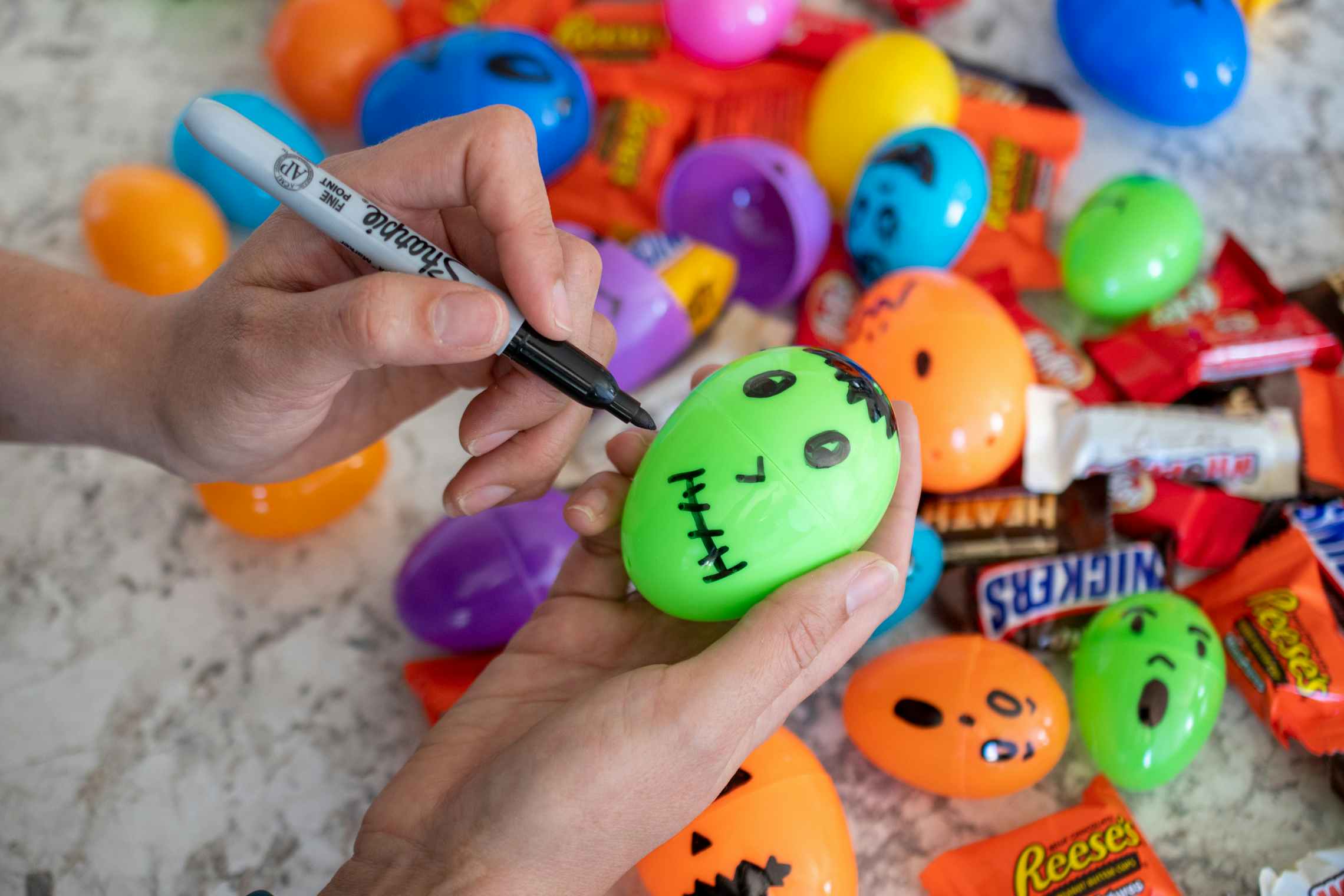 A woman using a sharpie to draw monster faces on plastic Easter eggs.