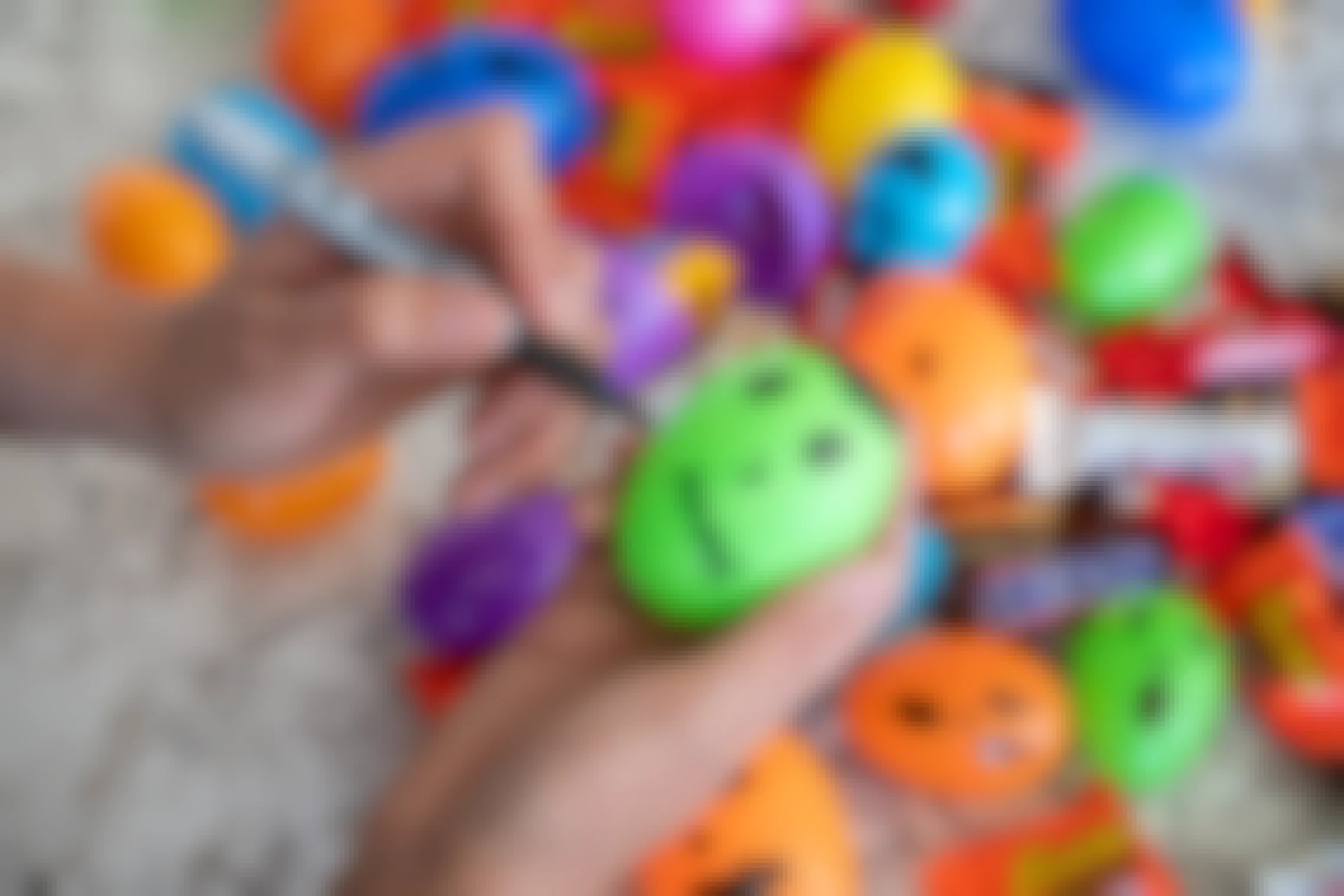 A woman using a sharpie to draw monster faces on plastic Easter eggs.