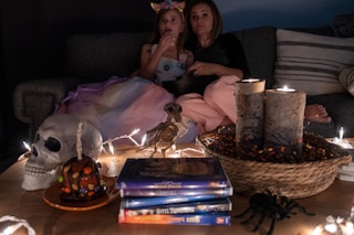 A woman and child eating popcorn watching a movie, with a table filled with treats, candles, and other halloween kids movies.