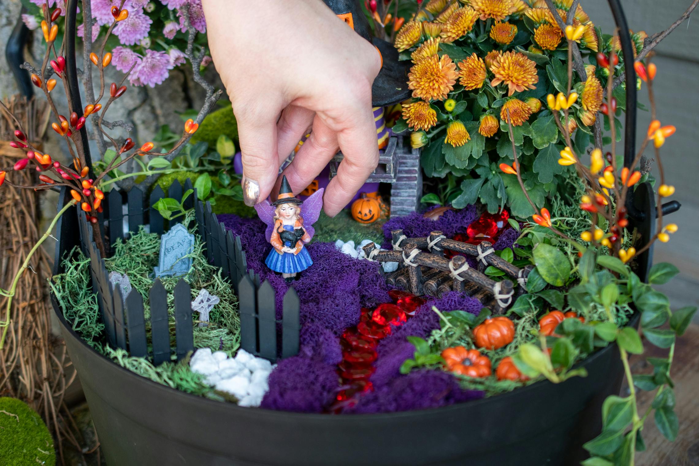 A woman putting a small fairy witch into a Halloween themed fairy garden