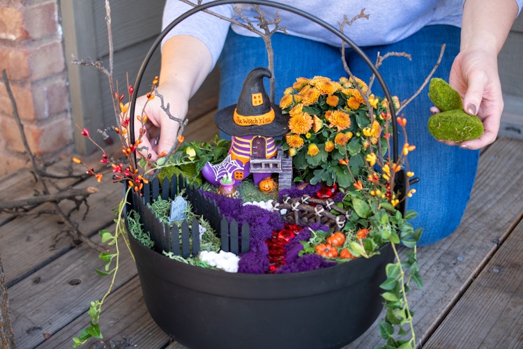 A woman putting faux moss stones into a Halloween fairy garden.