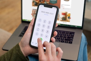 1-800 number on a cell phone with a laptop out of focus in the background.