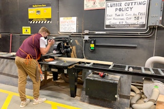 A home depot employee using an electric saw to cut lumber.