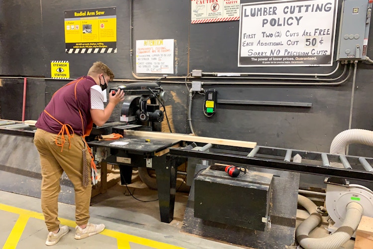 A home depot employee using an electric saw to cut lumber.